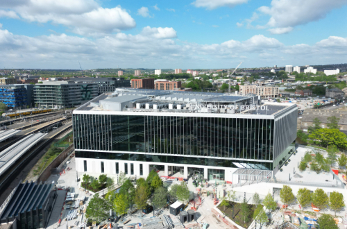 Drone photo of Temple Quarter Enterprise Campus main building with trees in foreground and blue skies, showcasing the University of Bristol signage